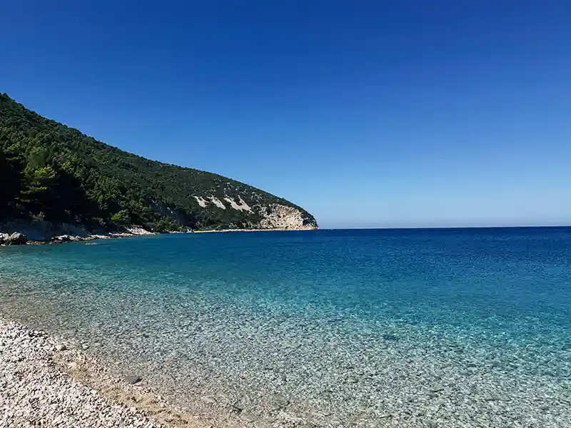 Isla de Sazan vista desde una lancha rápida, colinas verdes que se encuentran con el mar Jónico turquesa