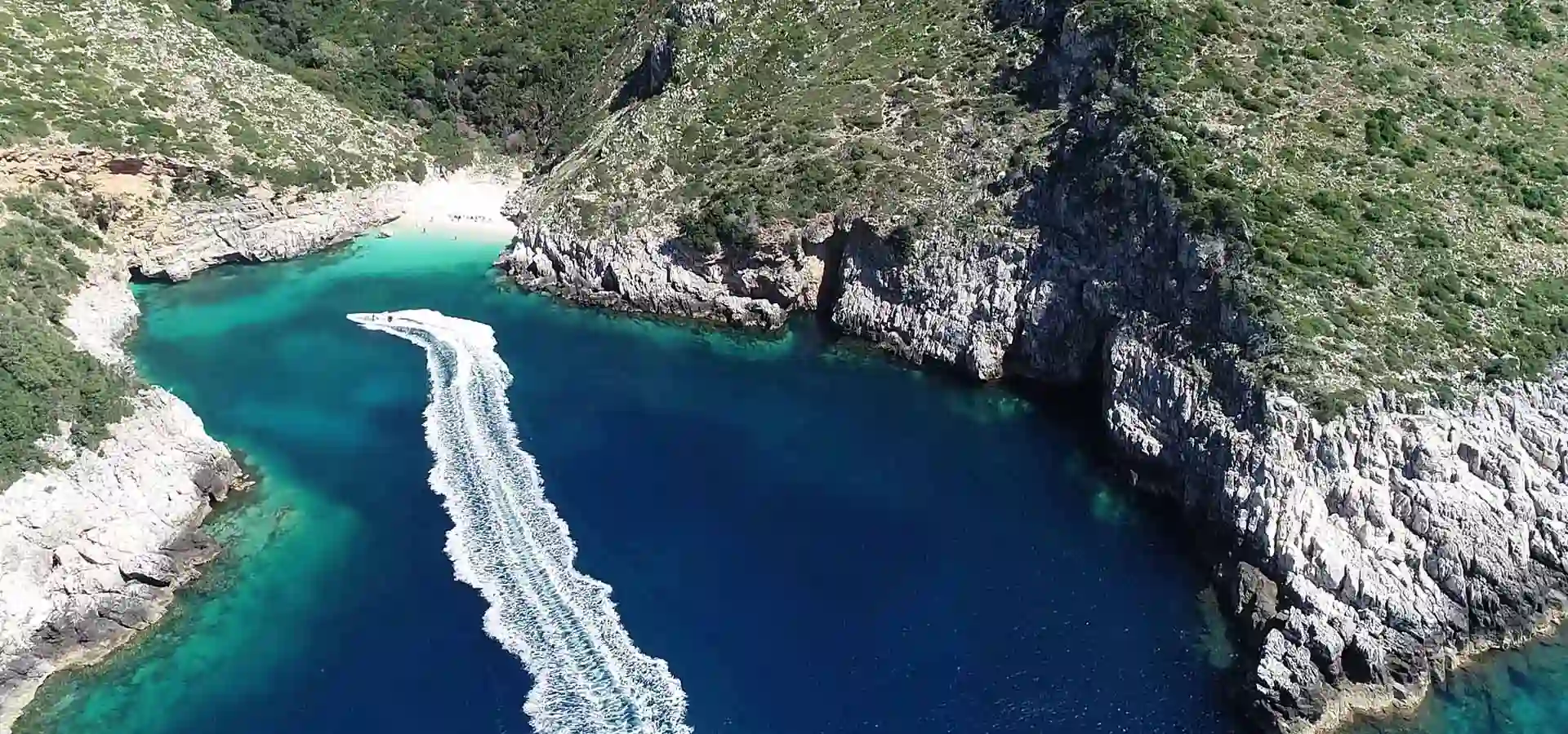 Aerial view of Dafina Bay with speedboat anchored in turquoise water beside a small pebble beach, Karaburun Peninsula Albania