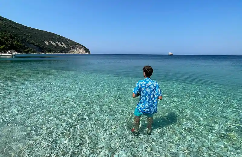 Vista de la costa de la Isla de Sazan desde el mar, colinas verdes que se encuentran con aguas turquesa del mar Jónico