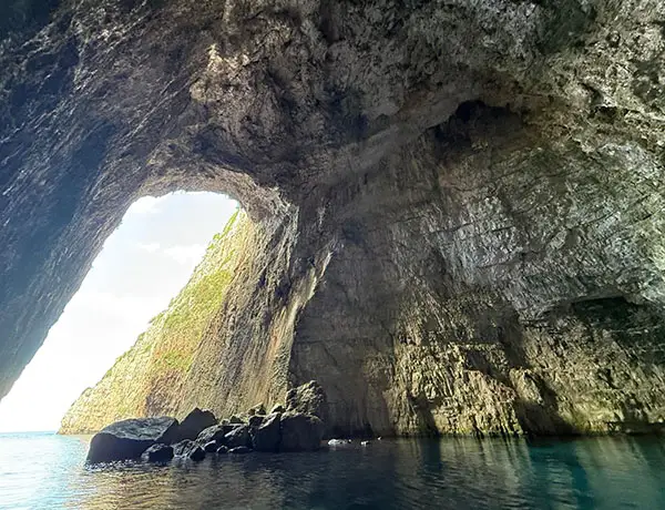 Entrée de la grotte de Haxhi Ali avec falaises calcaires impressionnantes au-dessus de la mer Ionienne turquoise