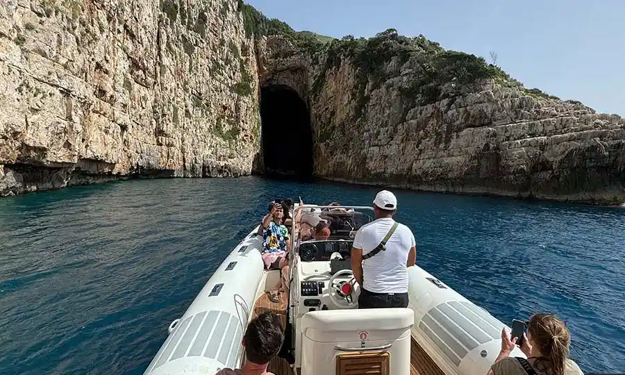 Motoscafo che entra nella Grotta di Haxhi Ali con arco calcareo imponente sopra acqua turchese, Penisola di Karaburun Albania