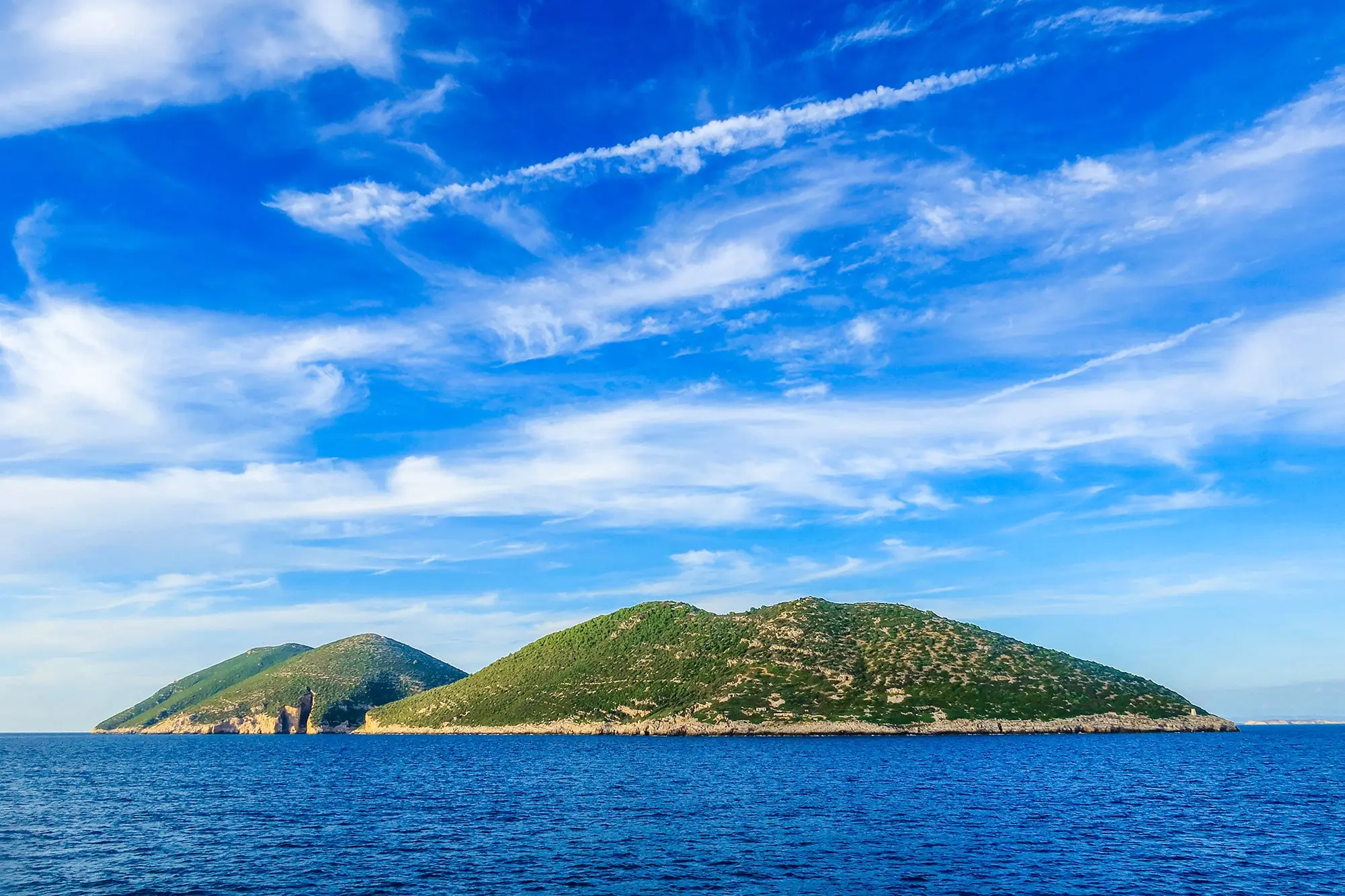 Southwestern side of sazan island seen from distance at sea. Short hills green vegetation and the sky in the background with sparse clouds